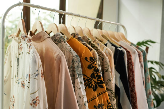 A row of assorted patterned blouses hanging on wooden hangers on a clothing rack