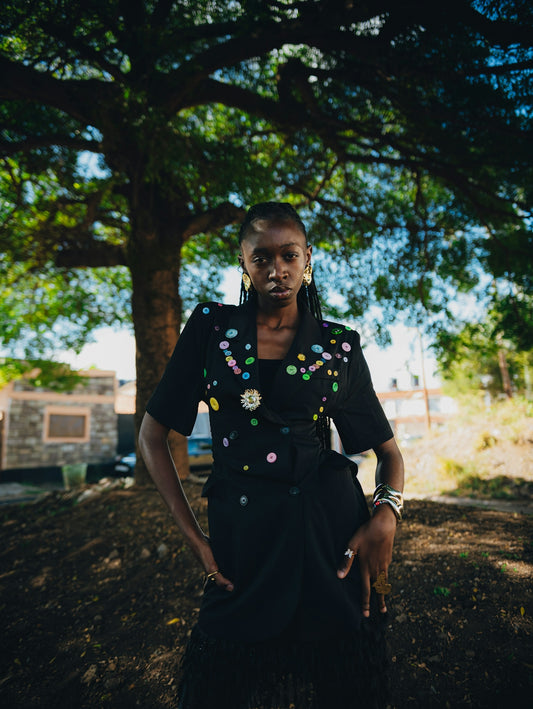 A black woman in a decorated black jacket stands outdoors.