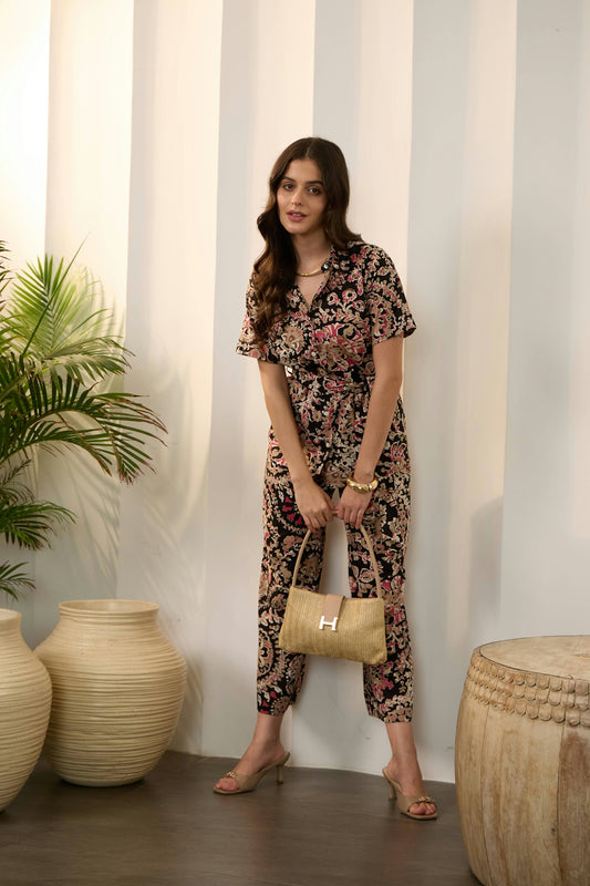 A woman in a patterned jumpsuit holds a straw handbag.