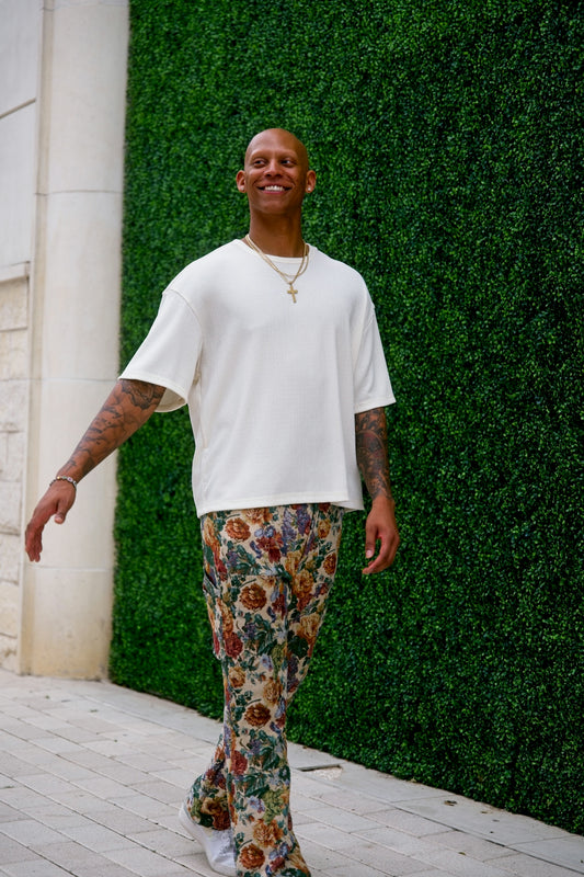 Man in patterned pants and white shirt walks outdoors.
