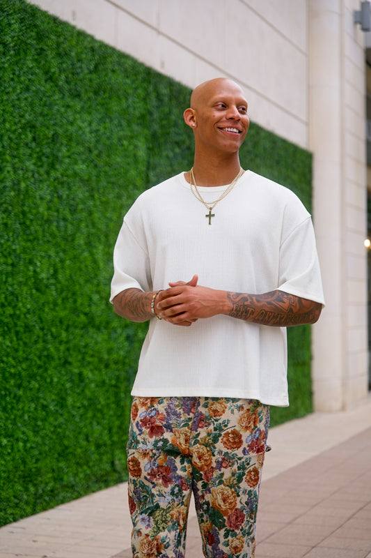 Bald man in white shirt and floral pants smiles.
