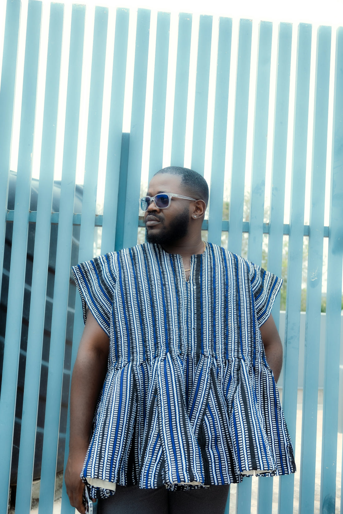 Man in traditional striped clothing stands by blue fence.
