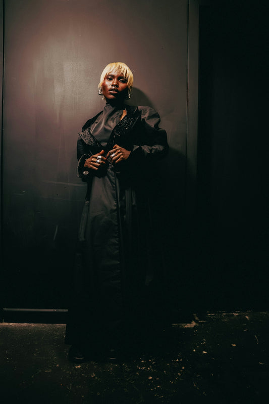 Blonde-haired figure in dark clothing against a dark background.